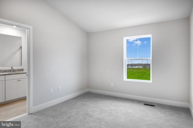 spare room featuring baseboards, visible vents, a sink, and light colored carpet