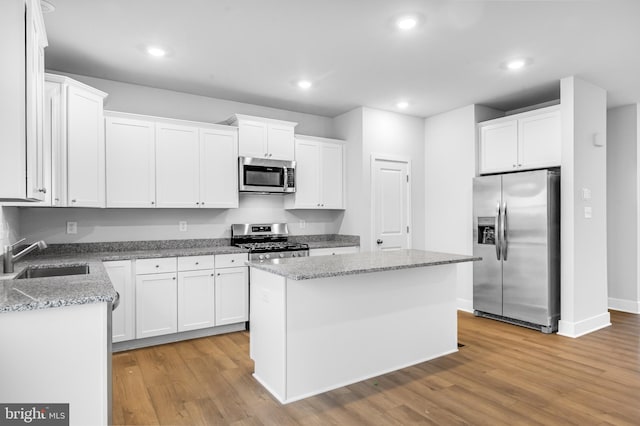 kitchen featuring a center island, a sink, white cabinetry, light wood-style flooring, and appliances with stainless steel finishes