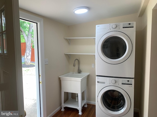 washroom featuring dark wood-style floors, baseboards, stacked washer / dryer, and laundry area