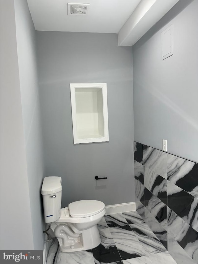 half bath with toilet, marble finish floors, and baseboards
