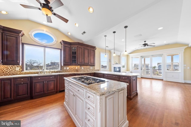 kitchen with light wood finished floors, stainless steel gas stovetop, a ceiling fan, a peninsula, and vaulted ceiling