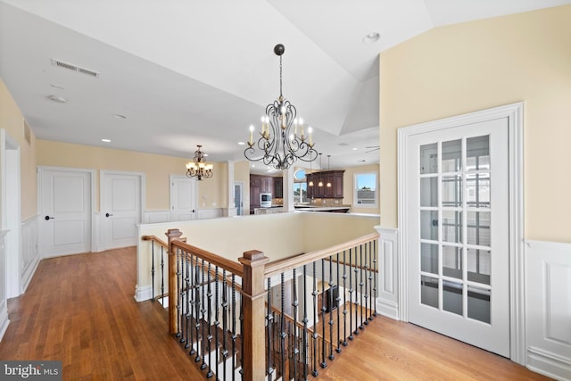 hallway featuring lofted ceiling, wood finished floors, a chandelier, and an upstairs landing