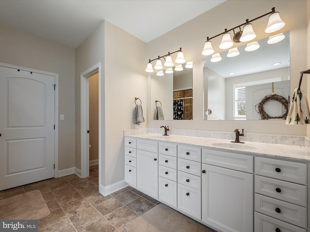 full bathroom with stone finish floor, baseboards, a sink, and double vanity