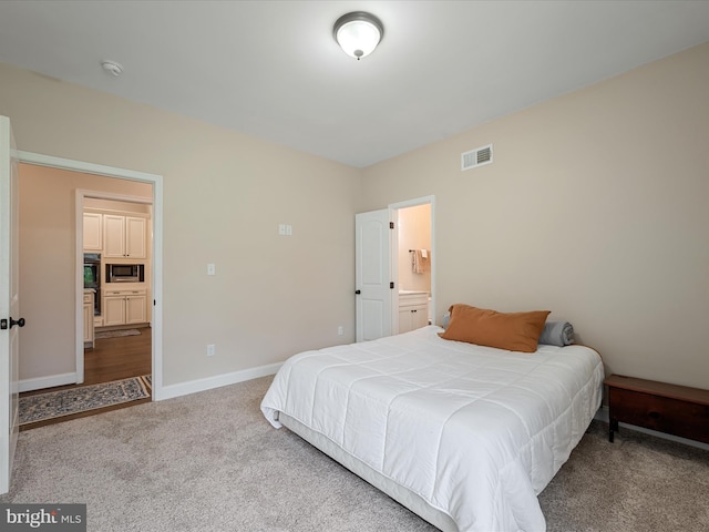 carpeted bedroom featuring baseboards, ensuite bathroom, and visible vents