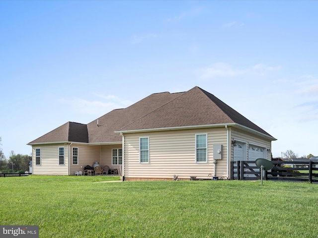 rear view of property featuring fence, a lawn, a shingled roof, and an attached garage