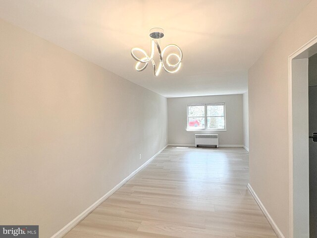 interior space featuring light wood-type flooring, baseboards, a notable chandelier, and radiator
