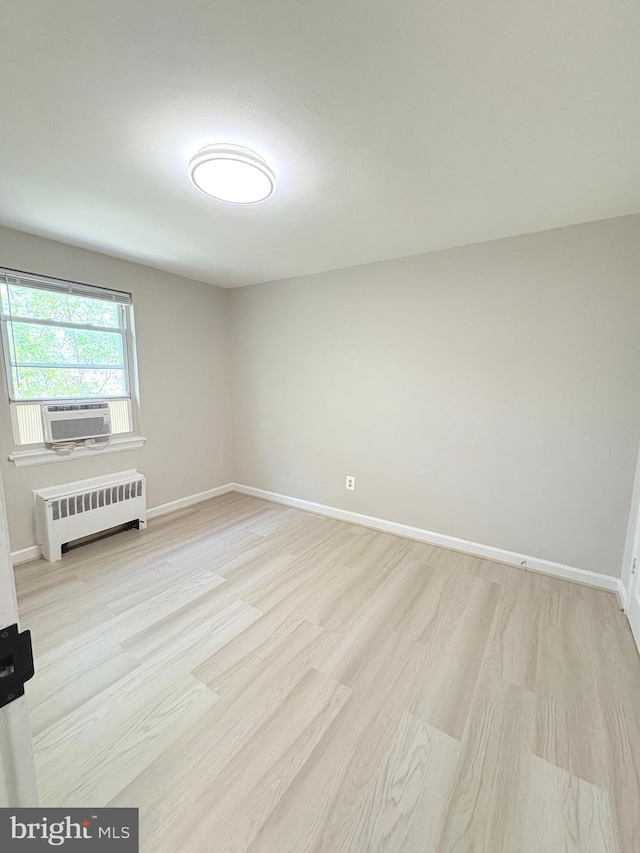 unfurnished room with radiator heating unit, cooling unit, baseboards, and light wood-style floors