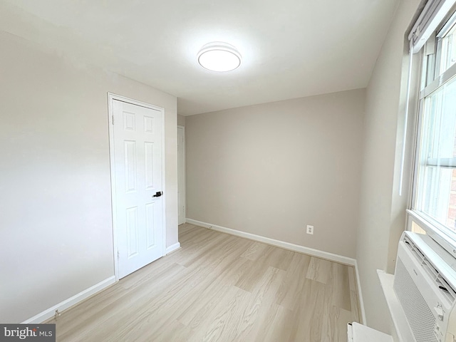 empty room featuring baseboards, a wall unit AC, and light wood-style flooring