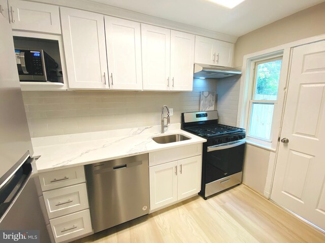 kitchen with stainless steel appliances, a sink, light wood-type flooring, white cabinetry, and under cabinet range hood