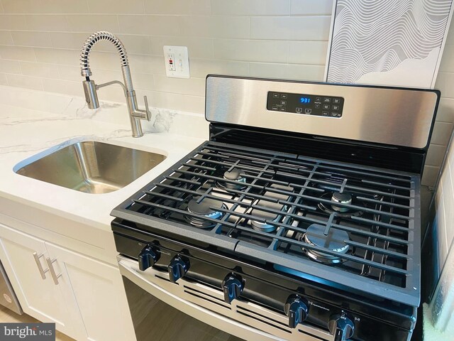 details with white cabinets, a sink, stainless steel range with gas cooktop, light stone countertops, and tasteful backsplash