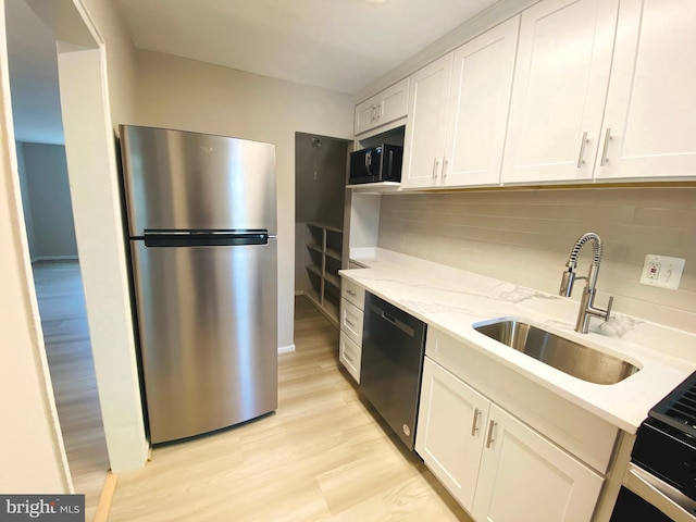 kitchen featuring dishwasher, a sink, freestanding refrigerator, black microwave, and white cabinetry