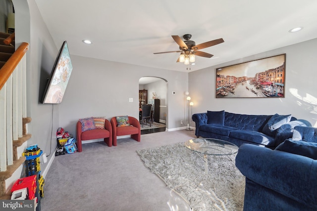 living room featuring arched walkways, carpet flooring, stairway, and ceiling fan