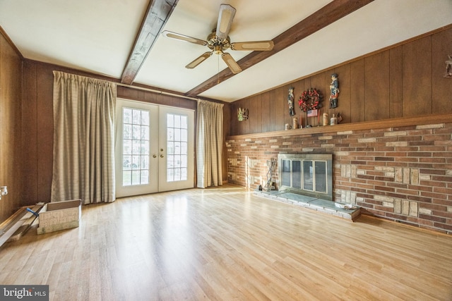 unfurnished living room featuring beam ceiling, wooden walls, french doors, wood finished floors, and ceiling fan