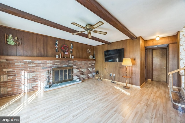 unfurnished living room with beamed ceiling, a ceiling fan, wooden walls, wood finished floors, and a brick fireplace