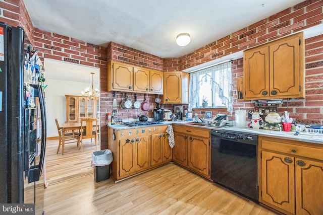 kitchen with black appliances, light wood-style floors, a chandelier, light countertops, and brick wall