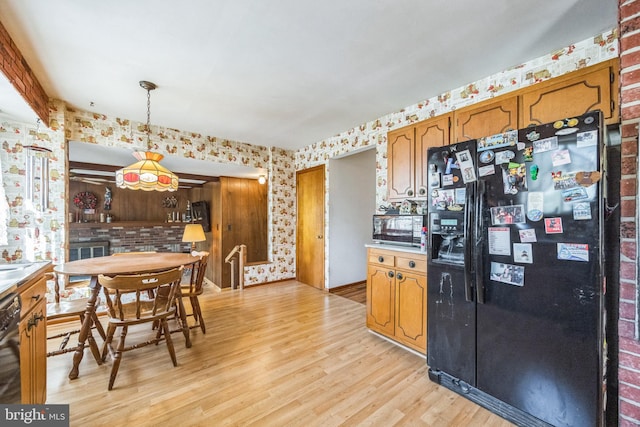 kitchen with black appliances, wallpapered walls, light wood finished floors, hanging light fixtures, and brown cabinetry