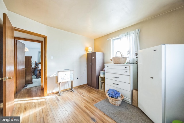 bedroom with freestanding refrigerator, light wood-type flooring, and baseboards