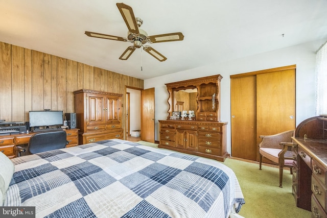 bedroom with a closet, an office area, ceiling fan, wood walls, and light colored carpet