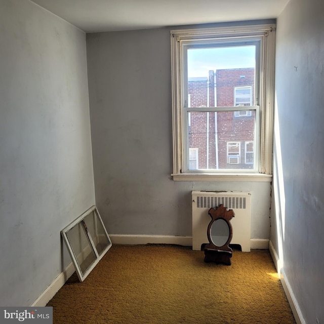 carpeted spare room featuring baseboards and radiator heating unit