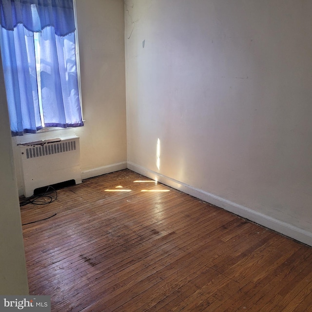 unfurnished room with hardwood / wood-style flooring, baseboards, and radiator