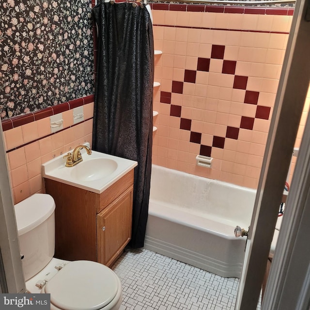 full bathroom featuring wallpapered walls, wainscoting, shower / bathtub combination with curtain, toilet, and vanity
