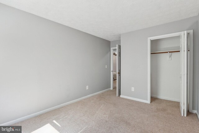unfurnished bedroom featuring a textured ceiling, baseboards, light carpet, and a closet