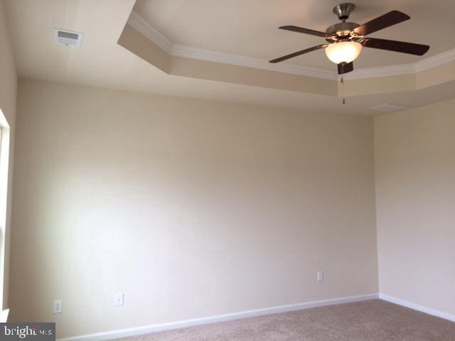 carpeted empty room with ceiling fan, a raised ceiling, baseboards, visible vents, and ornamental molding