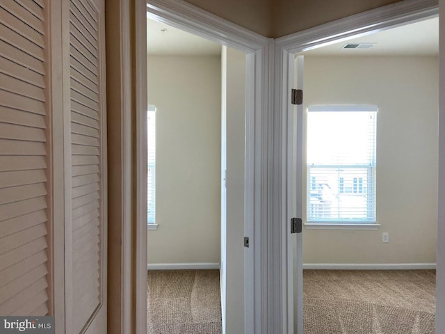 hallway featuring visible vents, carpet flooring, and baseboards
