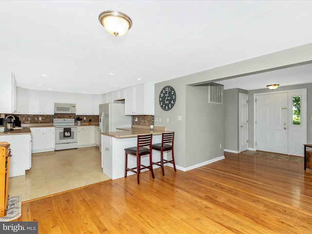 13240 Edgemont Rd, Smithsburg, MD 21783 - kitchen featuring white appliances, decorative backsplash, a breakfast bar, white cabinetry, and a peninsula