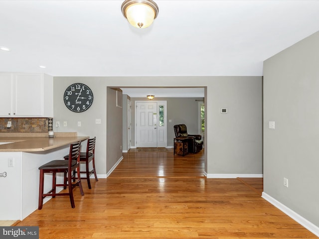 13240 Edgemont Rd, Smithsburg, MD 21783 - kitchen with a kitchen bar, white cabinetry, light wood-style floors, tasteful backsplash, and light countertops