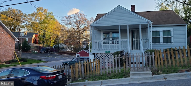 view of front of property with a fenced front yard, roof with shingles, a chimney, and covered porch