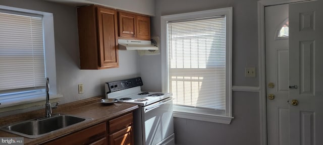 kitchen featuring under cabinet range hood, dark countertops, a sink, white range with electric cooktop, and brown cabinetry