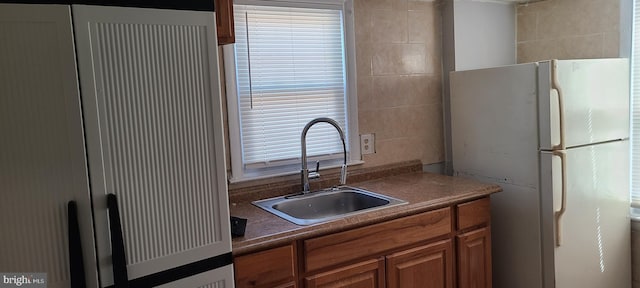 kitchen featuring brown cabinets, dark countertops, a sink, and freestanding refrigerator