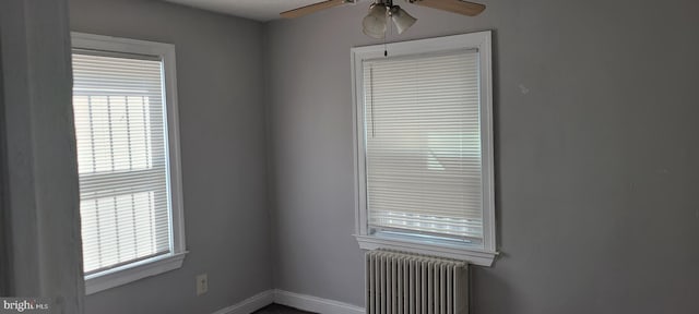 empty room with a ceiling fan, baseboards, radiator heating unit, and a healthy amount of sunlight