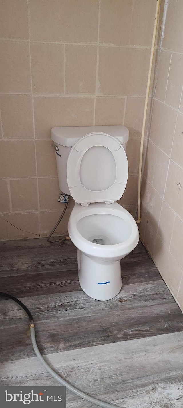 bathroom with concrete block wall, wood finished floors, and toilet