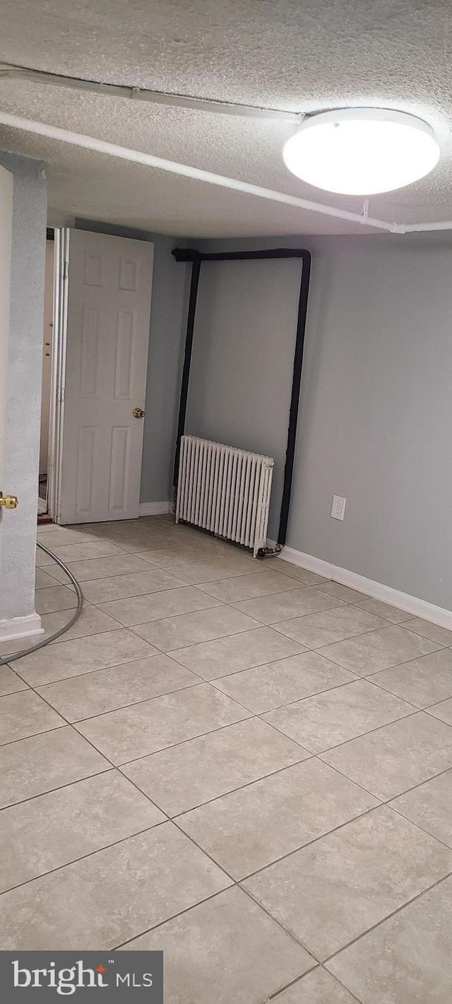 spare room with radiator heating unit, a textured ceiling, and baseboards