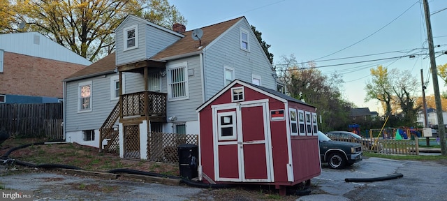 back of property with a chimney, fence, an outbuilding, and a shed