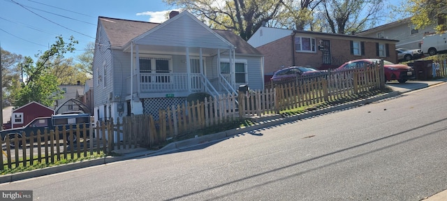 bungalow featuring covered porch, roof with shingles, a chimney, and a fenced front yard