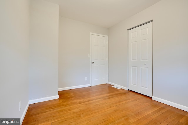 unfurnished bedroom featuring light wood-style flooring, a closet, and baseboards