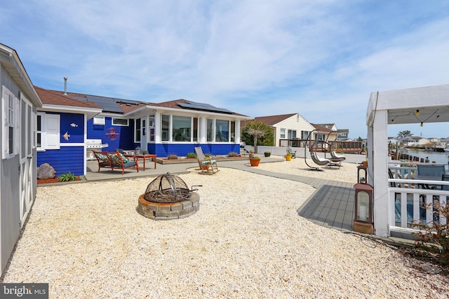 exterior space featuring an outdoor fire pit, a sunroom, solar panels, a patio area, and a playground
