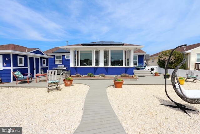 rear view of property with roof mounted solar panels, a patio area, and fence