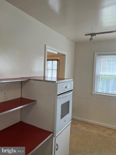 kitchen with white oven, baseboards, track lighting, and light tile patterned floors
