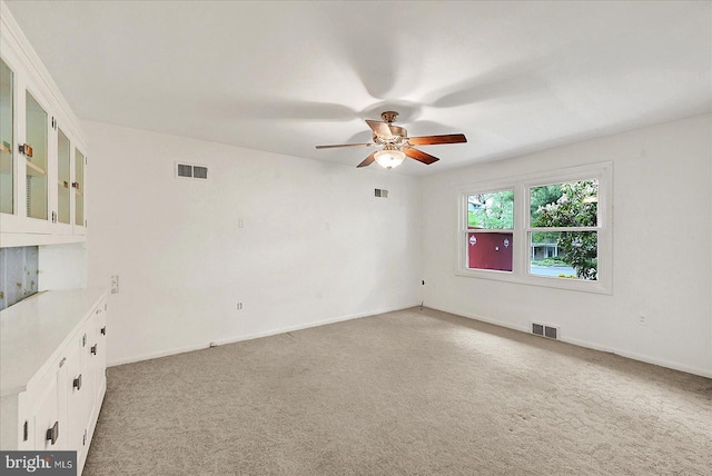 spare room with light colored carpet, a ceiling fan, and visible vents