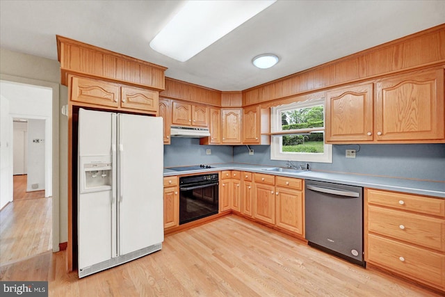 kitchen with a sink, black appliances, under cabinet range hood, light wood finished floors, and light countertops