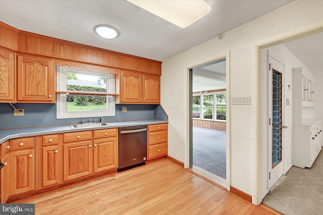 kitchen with light wood finished floors, light countertops, a sink, baseboards, and dishwasher