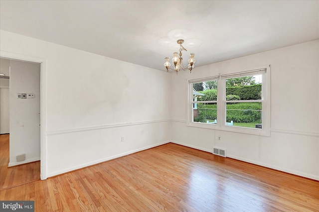 spare room featuring a chandelier, light wood-style flooring, baseboards, and visible vents