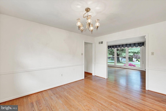 unfurnished room featuring baseboards, light wood-style floors, an inviting chandelier, and visible vents