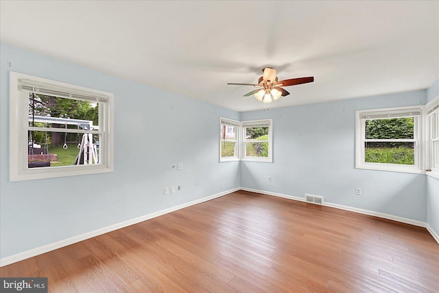 empty room featuring ceiling fan, baseboards, visible vents, and wood finished floors