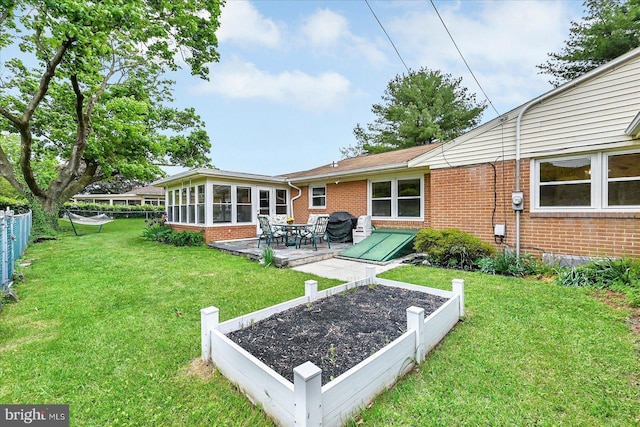 rear view of property featuring fence, brick siding, a lawn, a sunroom, and a garden
