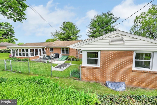 back of house with a patio area, brick siding, a fenced backyard, a lawn, and a sunroom